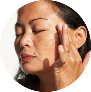 Person gently applying skincare product to their cheek with eyes closed.