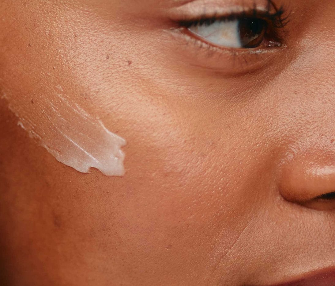 Close-up of a person's face with a smear of white cream applied to their cheek near the eye.